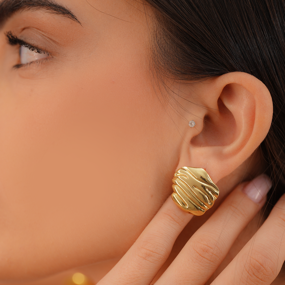 Close-up of a person wearing a gold earring with a hand touching the ear.