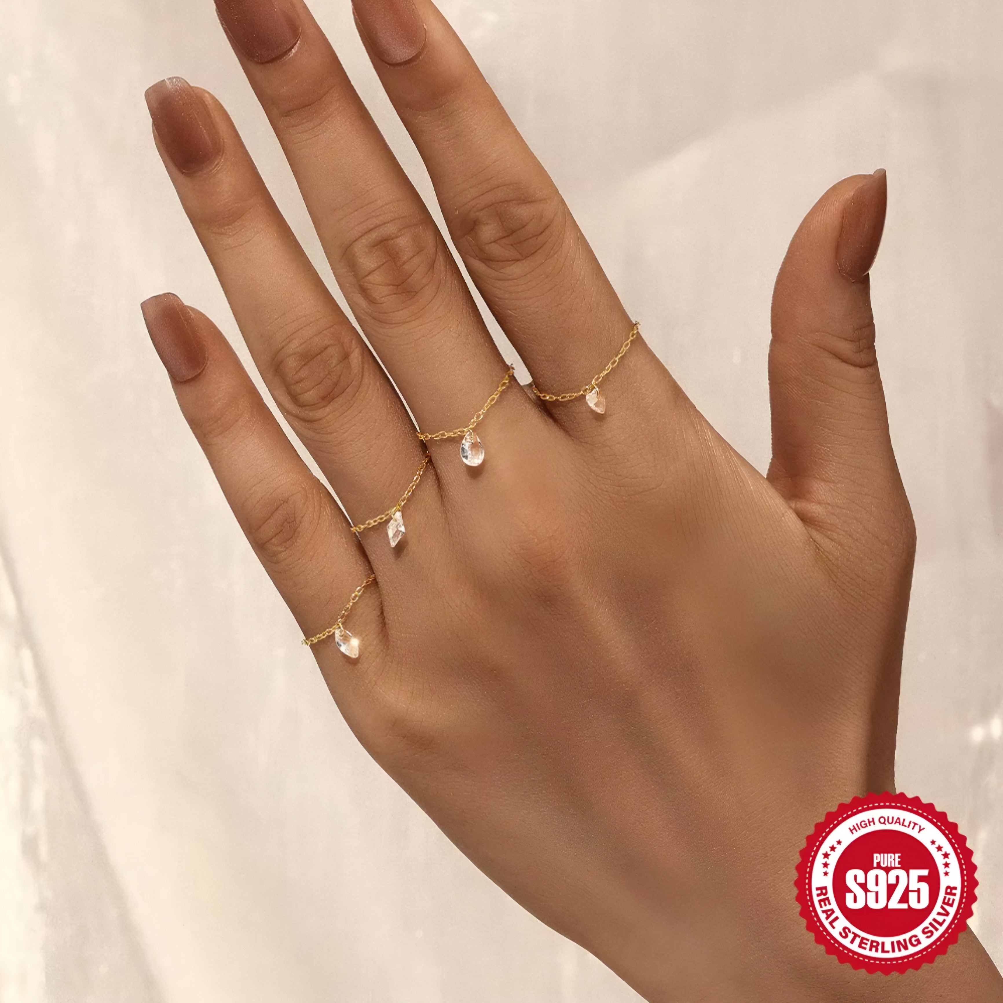 Hand wearing gold rings with a '925 Sterling Silver' stamp on a neutral background