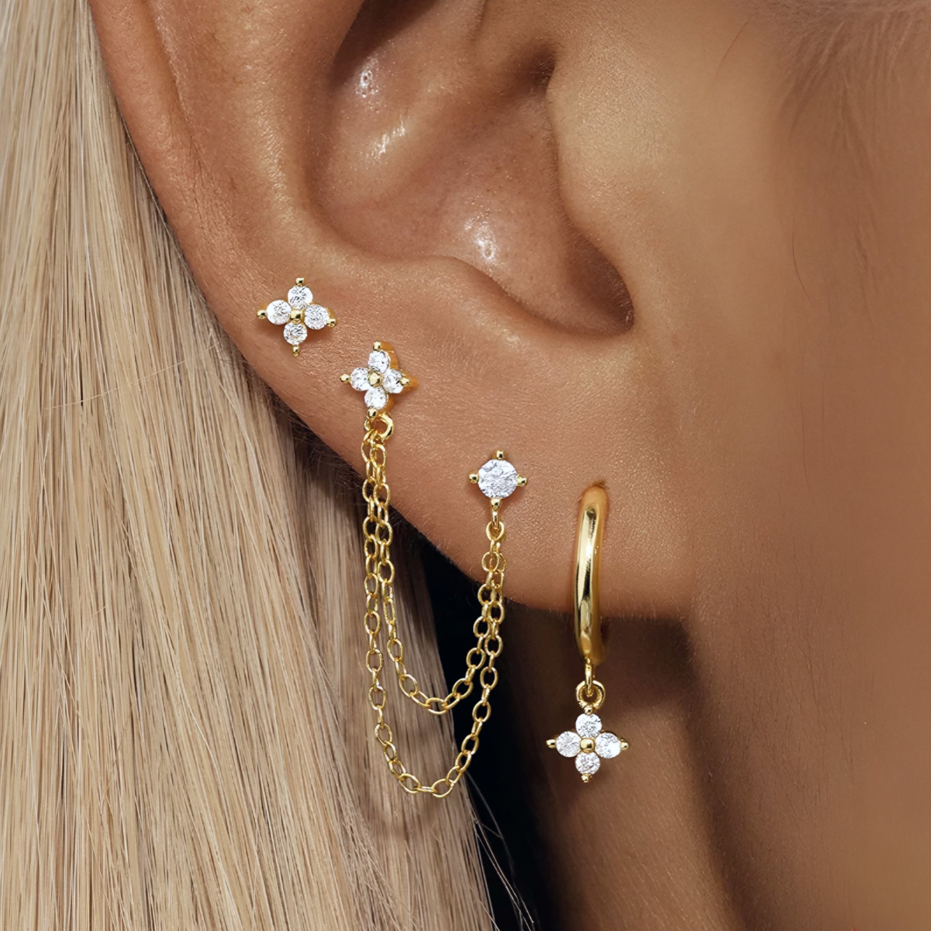 Gold earrings with floral designs worn on an ear