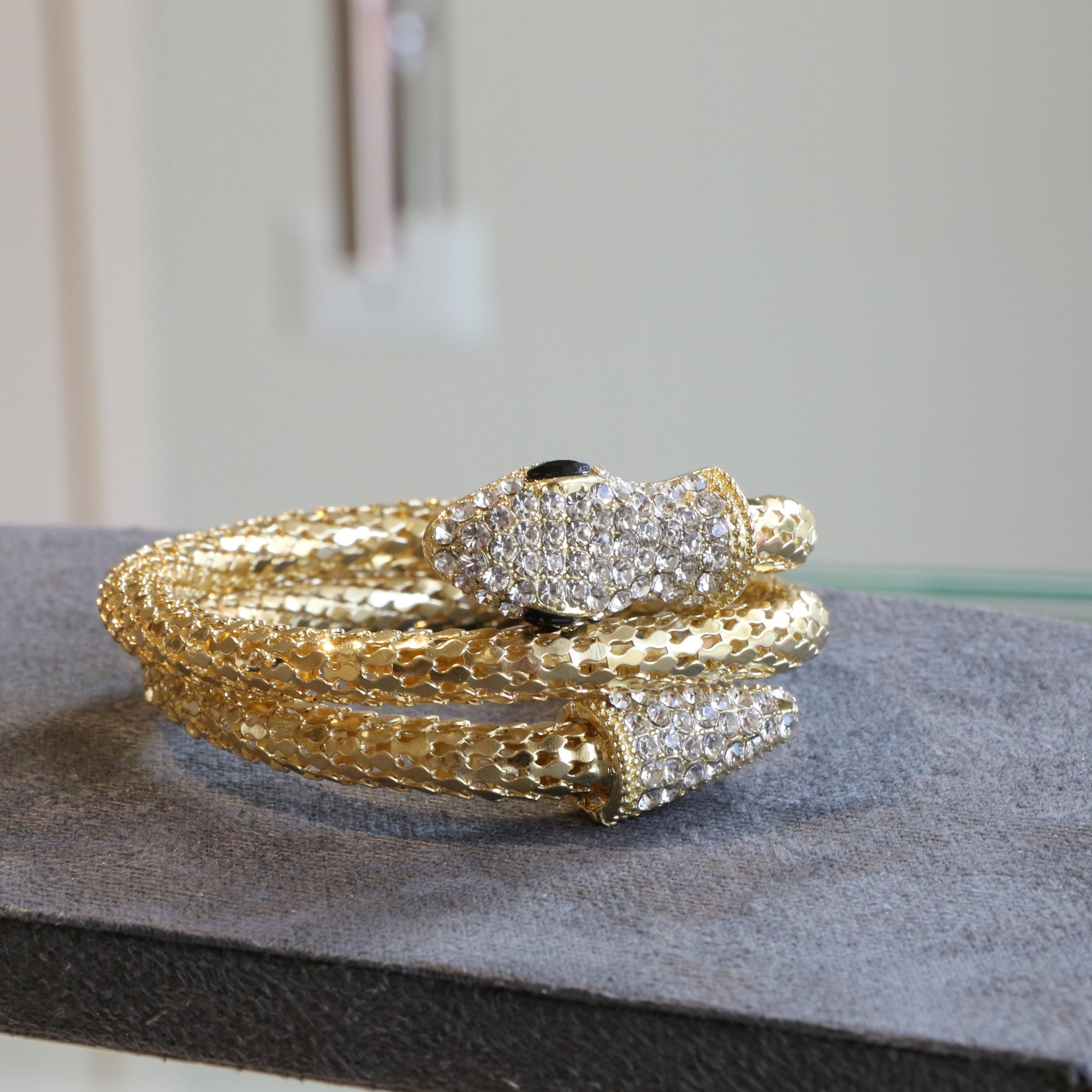 Gold and silver snake-shaped bracelet on a gray surface with a blurred background