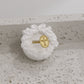 Gold ring with a cross design on a white textured stand against a light gray background