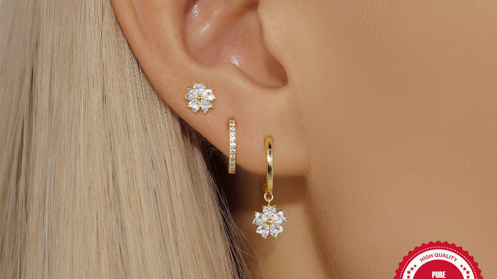 Close-up of an ear wearing gold hoop earrings with floral designs, with a '925 Sterling Silver' stamp in the corner.