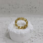 Gold braided ring on a white pedestal against a gray background