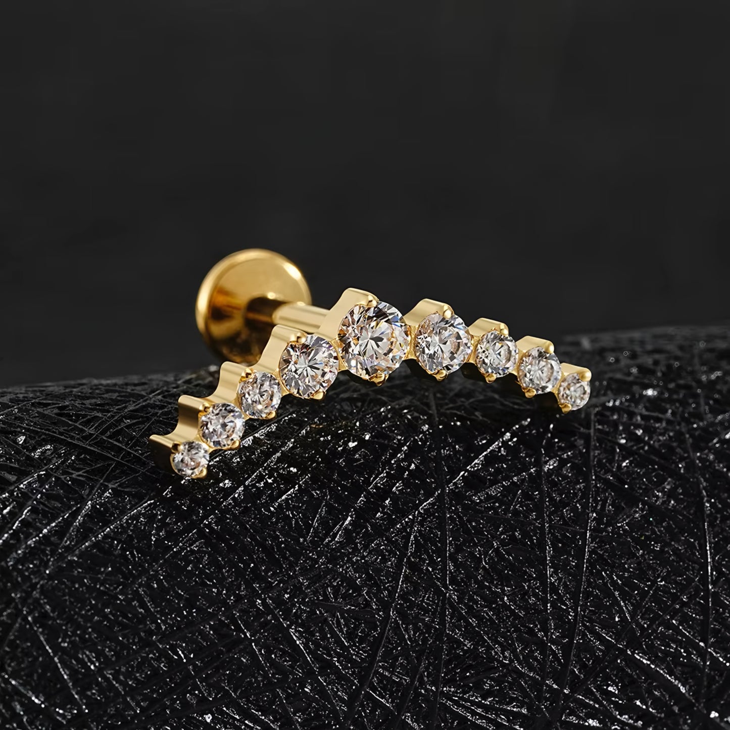 Gold earring with diamonds on a black textured surface