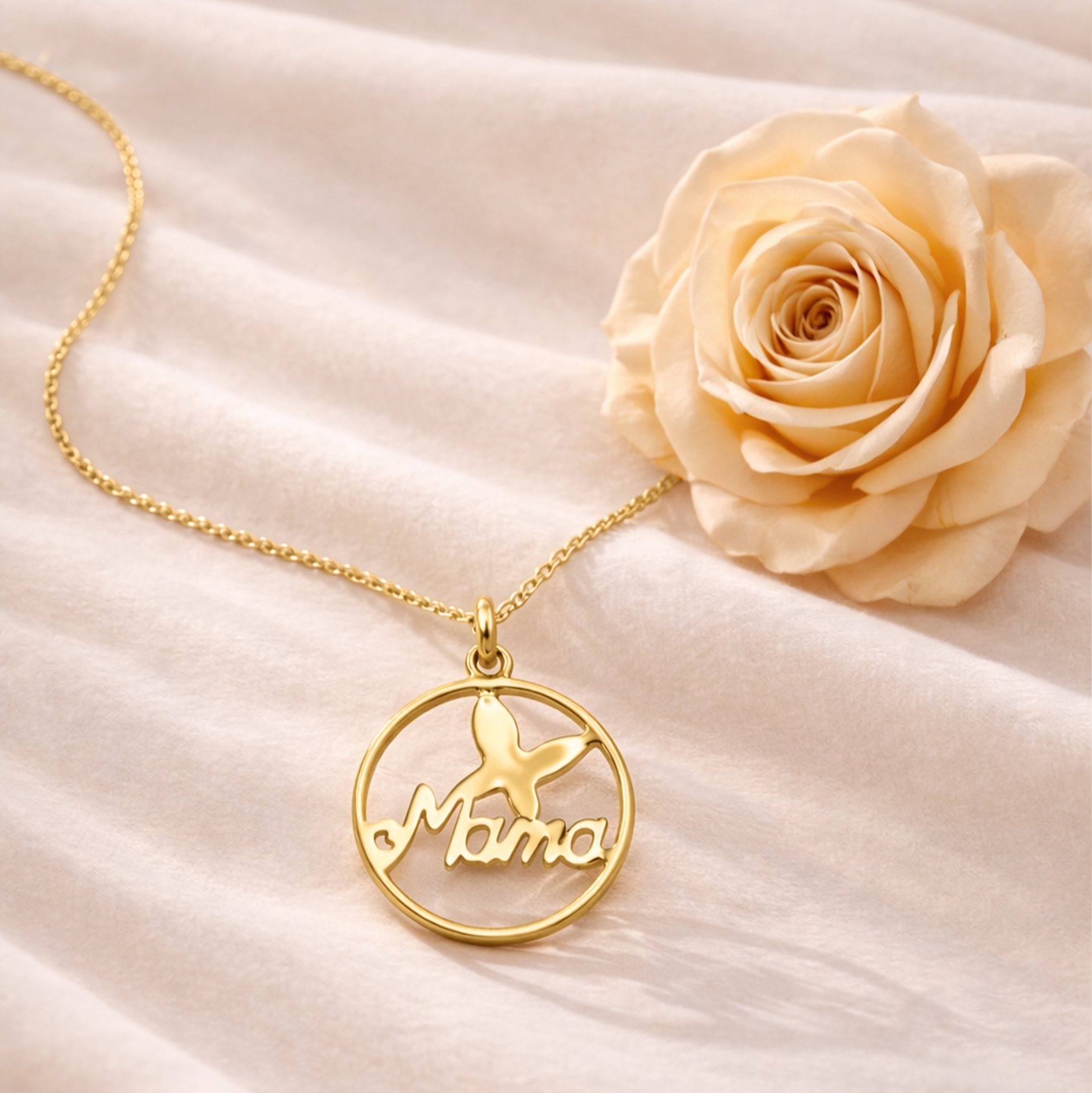 Gold necklace with 'Mama' pendant on a soft fabric background with a rose.