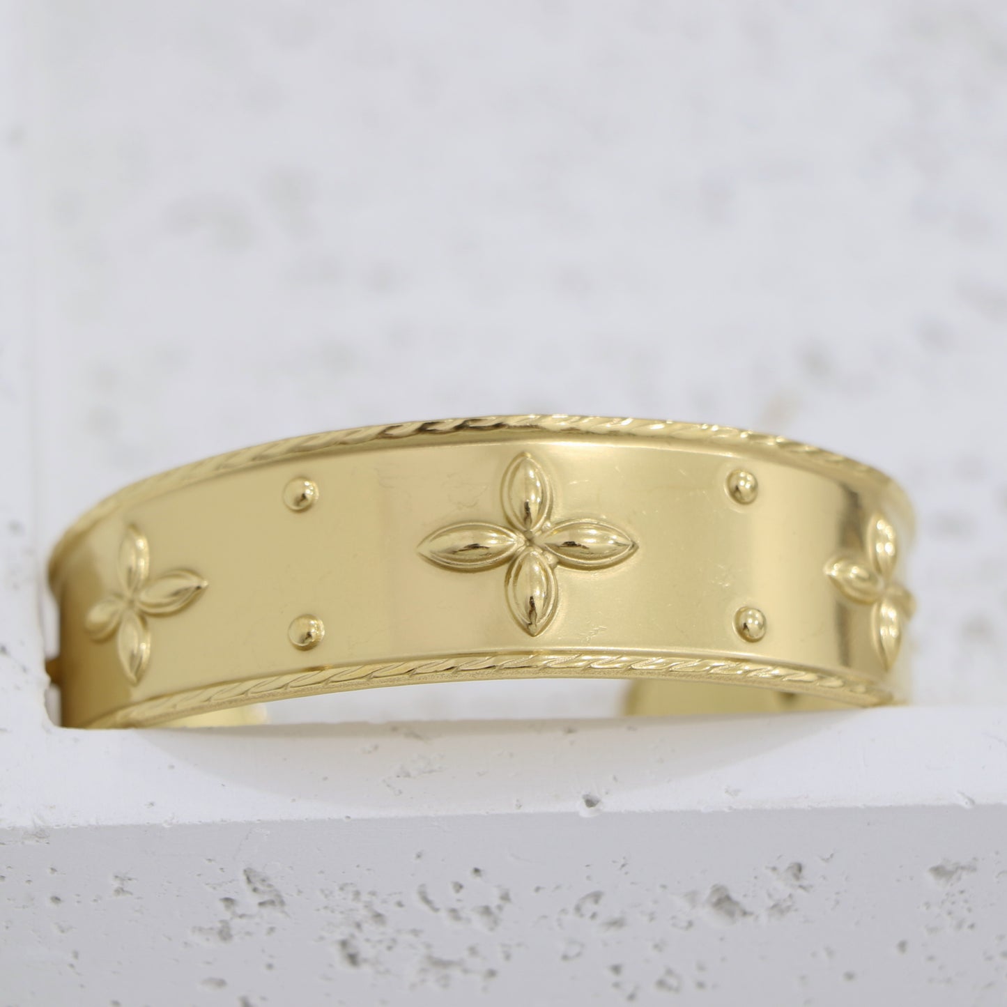 Gold bracelet with floral patterns on a light gray background
