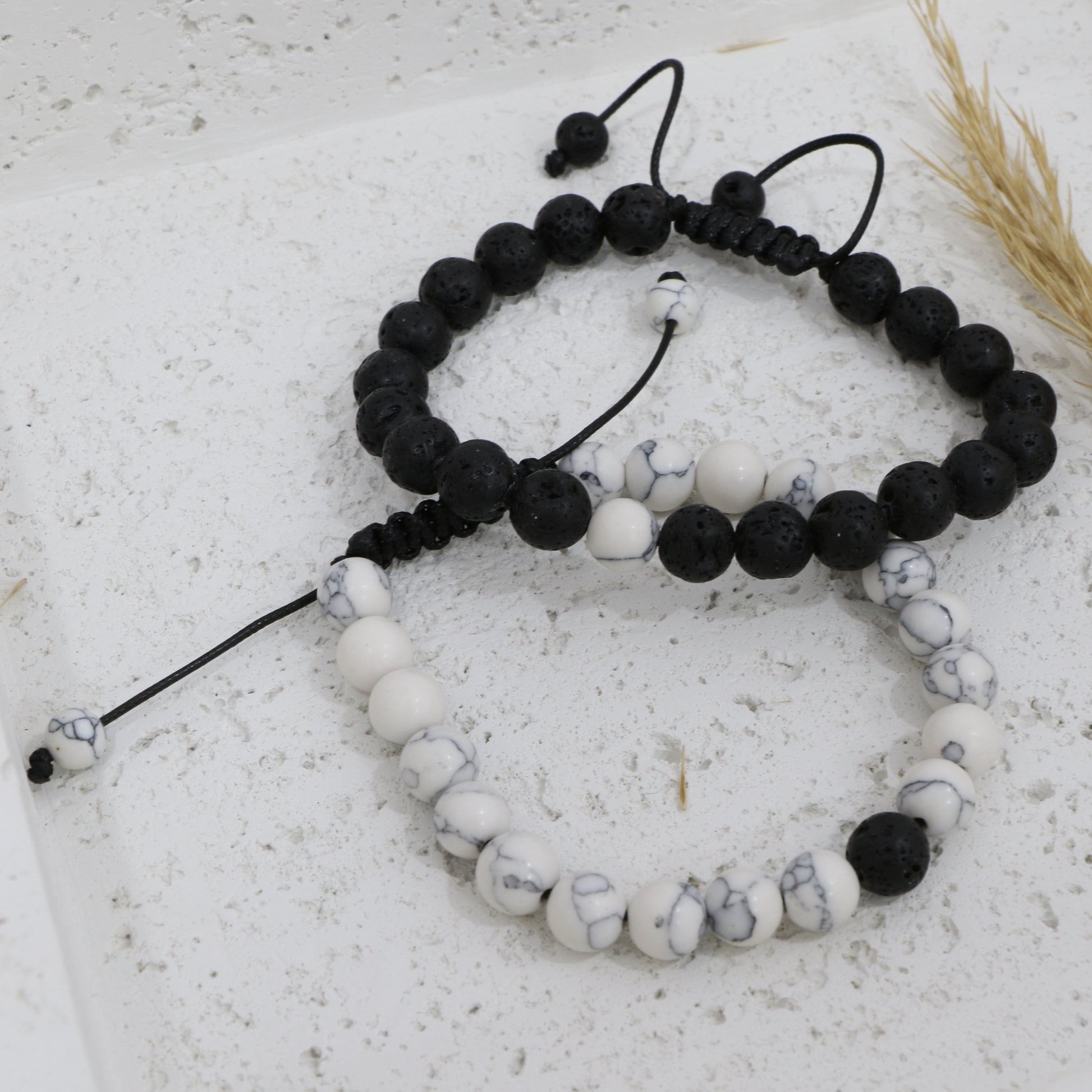 Two beaded bracelets, one black and one with a mix of black and white beads, on a textured surface.