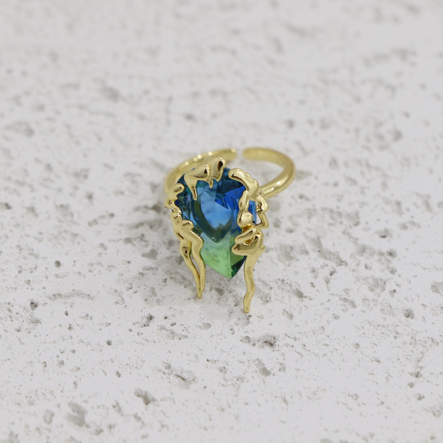 Gold ring with a blue and green gemstone on a textured gray background