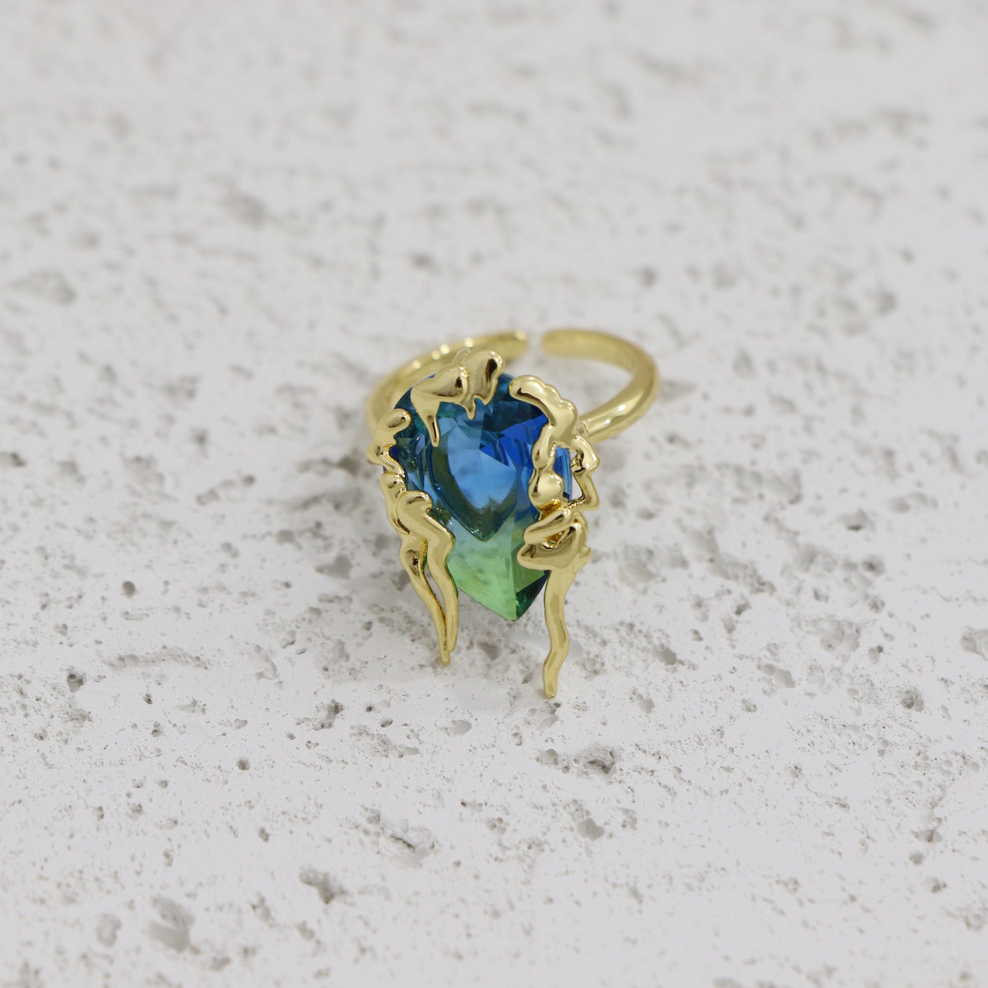 Gold ring with a blue and green gemstone on a textured gray background