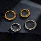 Four gold and silver hoop earrings on a dark stone surface
