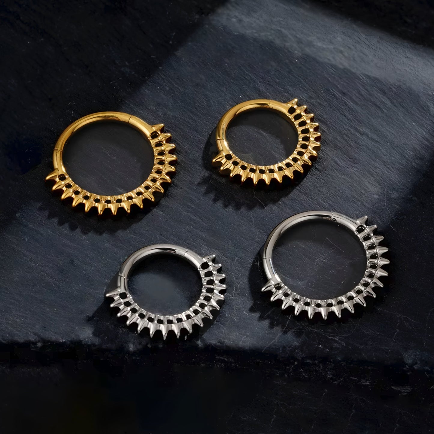 Four gold and silver hoop earrings on a dark stone surface