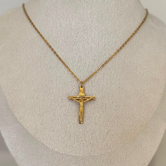 A gold crucifix pendant necklace on a textured cream fabric mannequin bust.