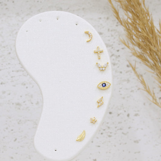 Set of gold earrings on a white stone surface with natural elements.