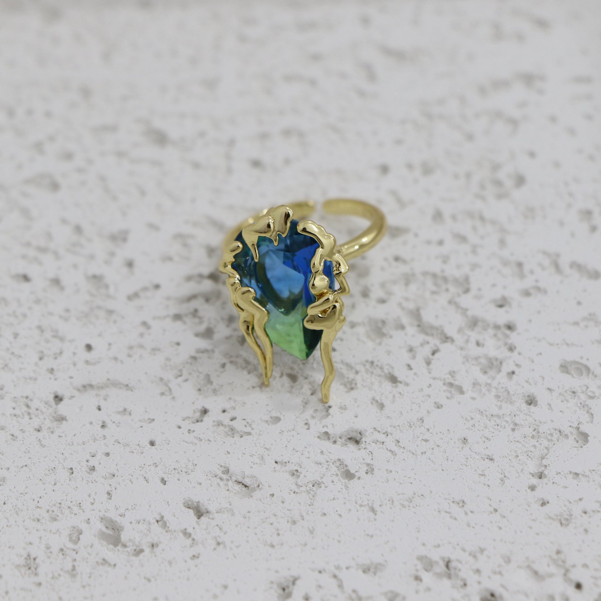 Gold earring with a blue gemstone on a light gray background