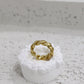 Gold twisted ring on a white pedestal against a gray background