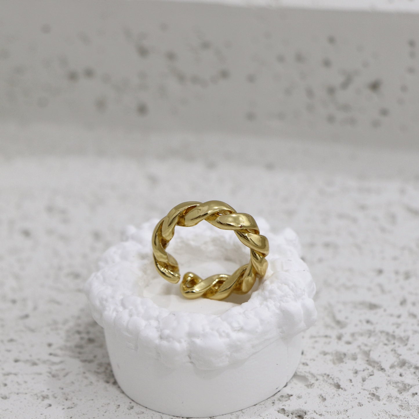 Gold twisted ring on a white pedestal against a gray background
