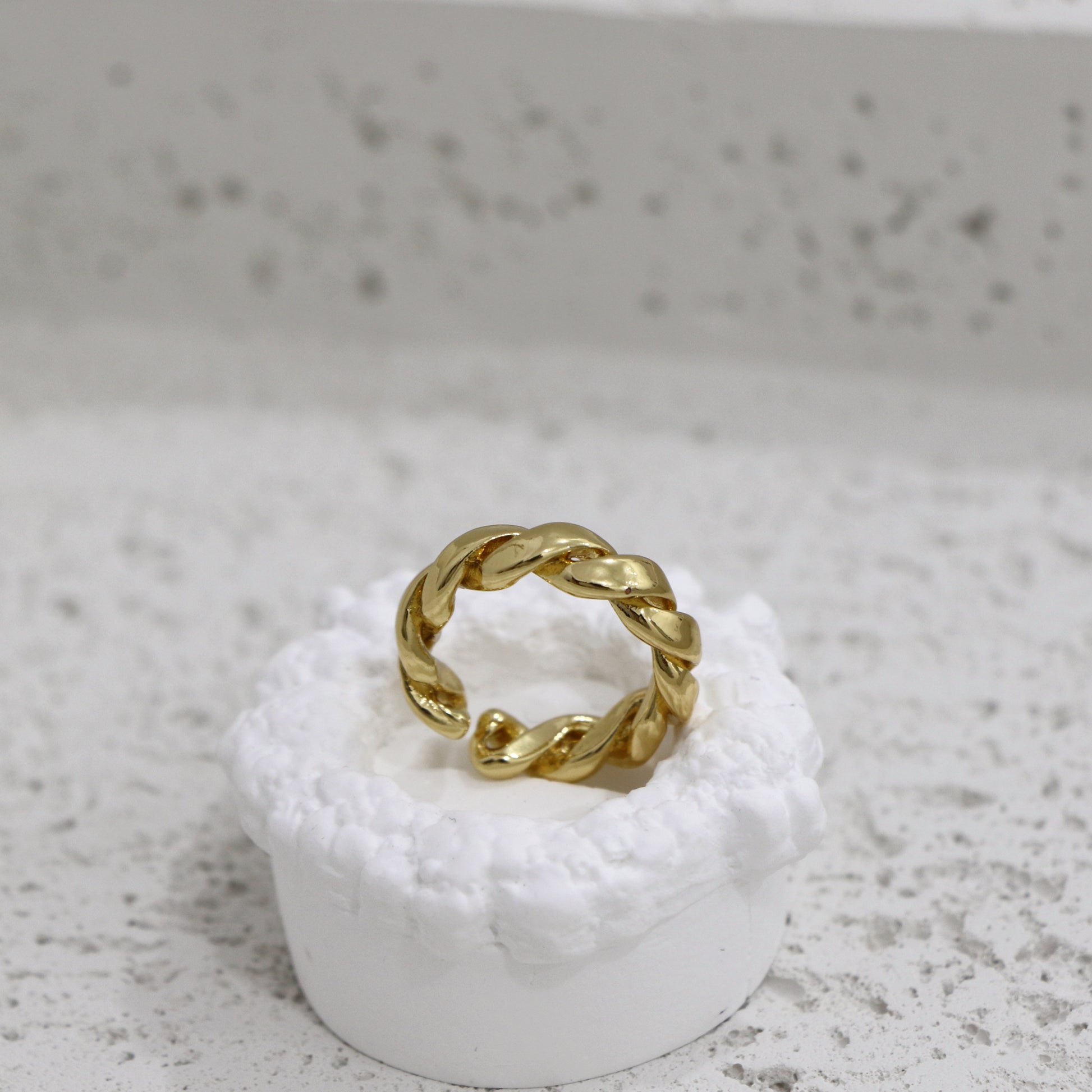 Gold twisted ring on a white pedestal against a gray background