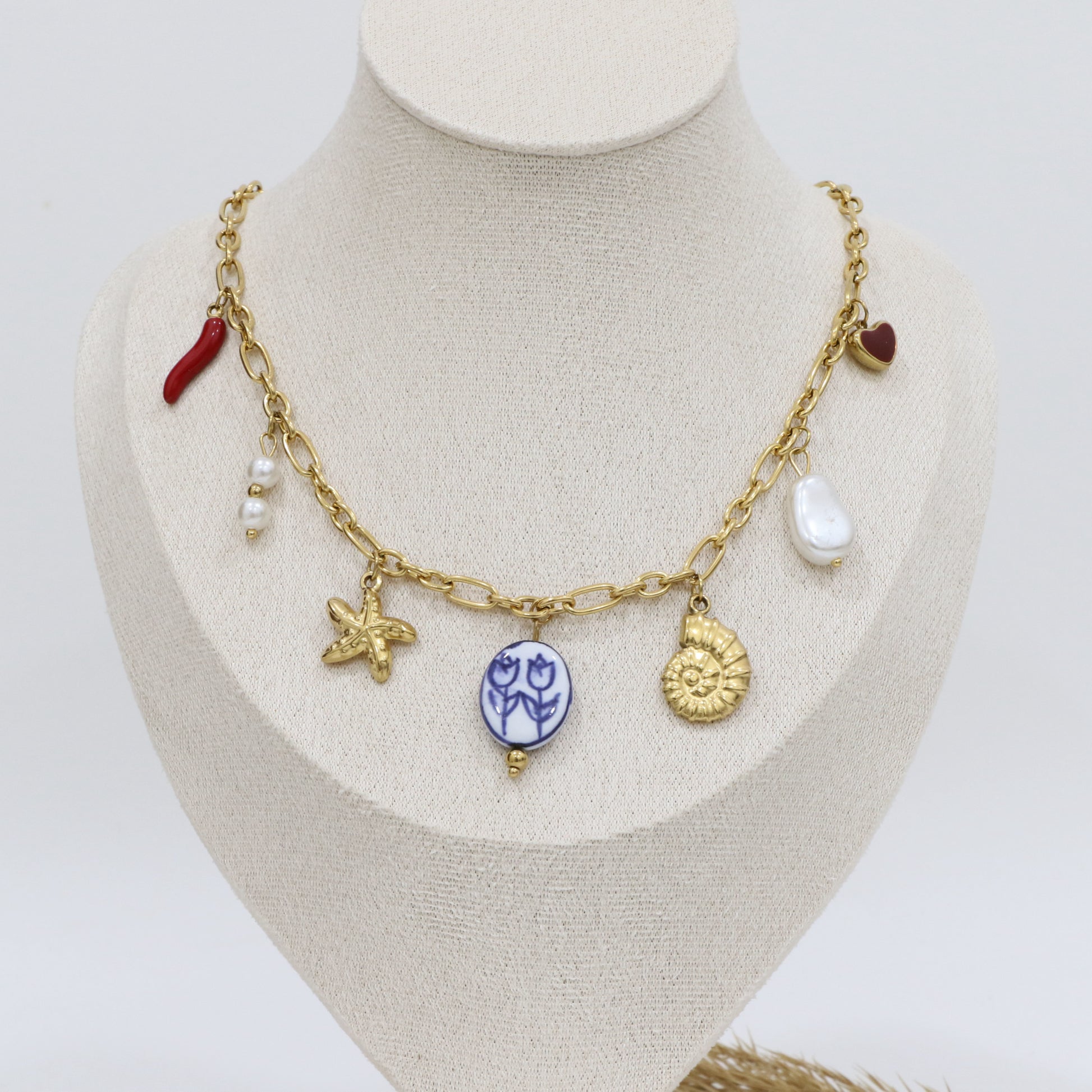 Gold necklace with various charms on a mannequin bust against a white background