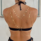 A gold chain back harness with hanging coin charms worn over a black bikini top, shown from the back on a model.