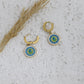 Gold hoop earrings with blue and green circular designs on a textured surface.