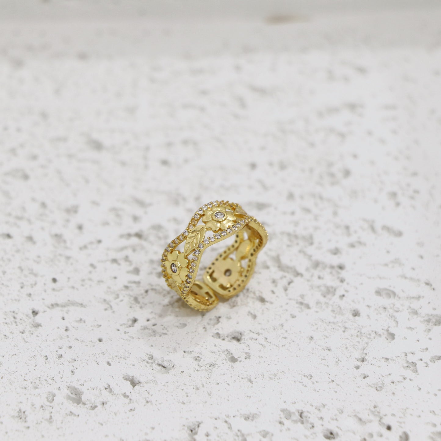 Gold ring with intricate design on a textured white surface
