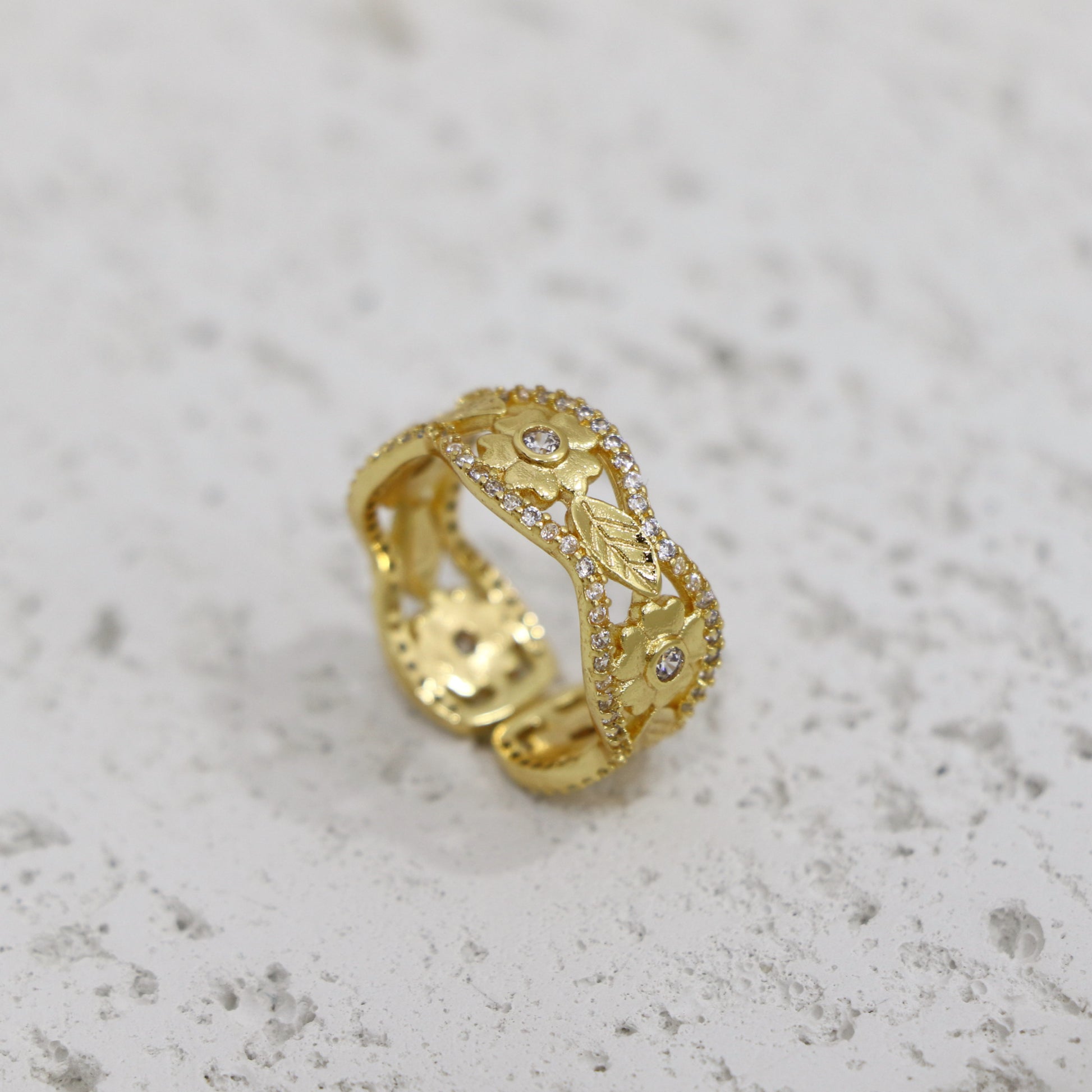 Gold ring with intricate design on a light gray surface