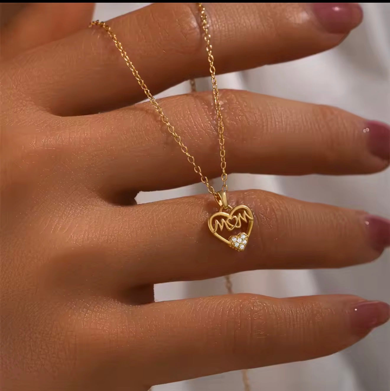 Gold necklace with a heart-shaped pendant on a hand against a white background mothers day gift