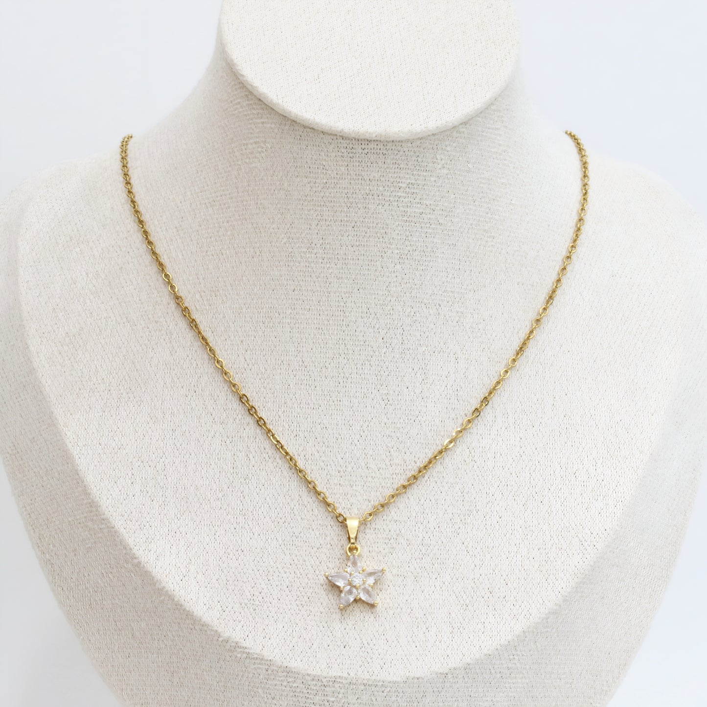 Gold necklace with a star-shaped pendant on a mannequin bust.