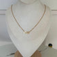 A delicate gold infinity necklace displayed on a textured cream-colored jewelry bust.