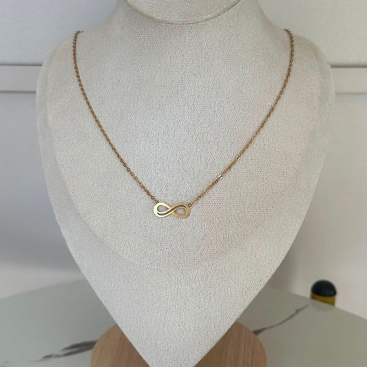 A delicate gold infinity necklace displayed on a textured cream-colored jewelry bust.