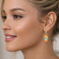 Close-up of a woman wearing colorful earrings with 'Kalopsisia' branding.